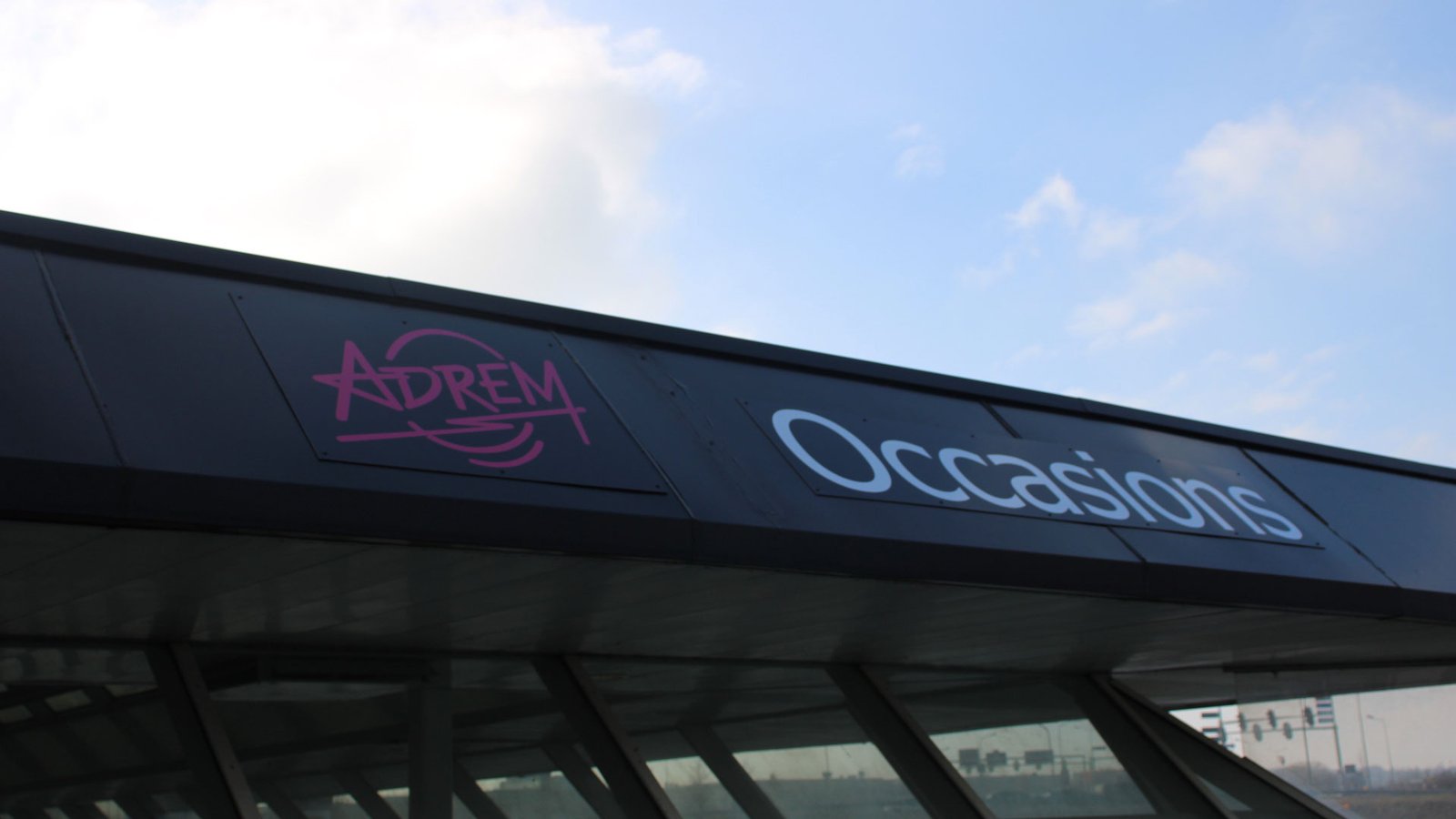 De luifel van Adrem Occasions in Maastricht met het logo tegen een blauwe lucht