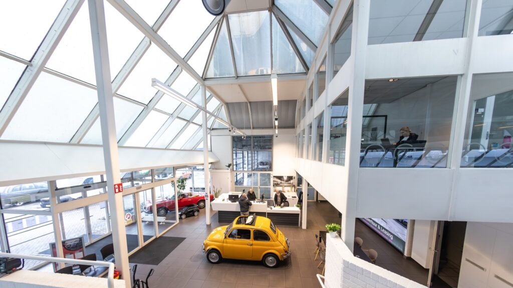 De showroom van Adrem Occasions in Maastricht, met een gele Fiat 500 onder het glazen dak